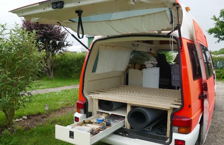 Offener Kofferraum eines Campingbusses mit Holzbett