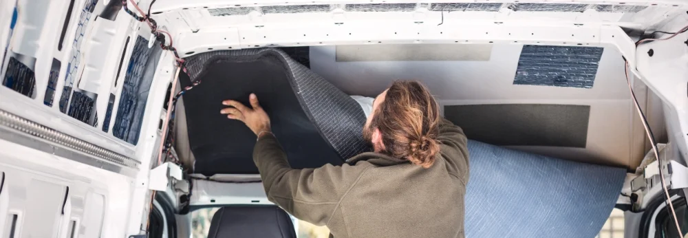 Person bringt Dämmmaterial in einem Fahrzeug an.