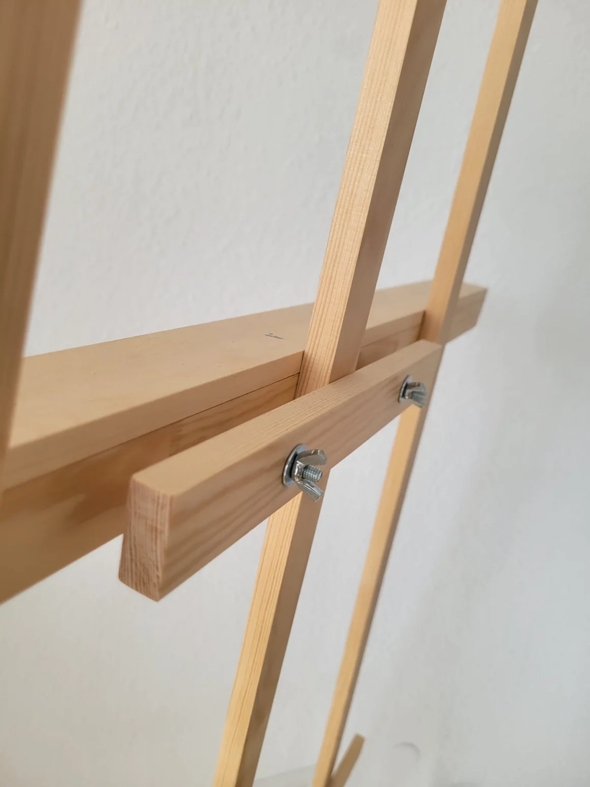 Nahaufnahme einer Holzstaffelei mit Schraubverbindungen und Flügelschrauben.