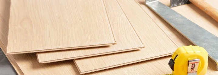 Mehrere Laminatplatten liegen auf einem Boden. Daneben liegen ein Zollstock, ein Bleistift und ein Hammer.