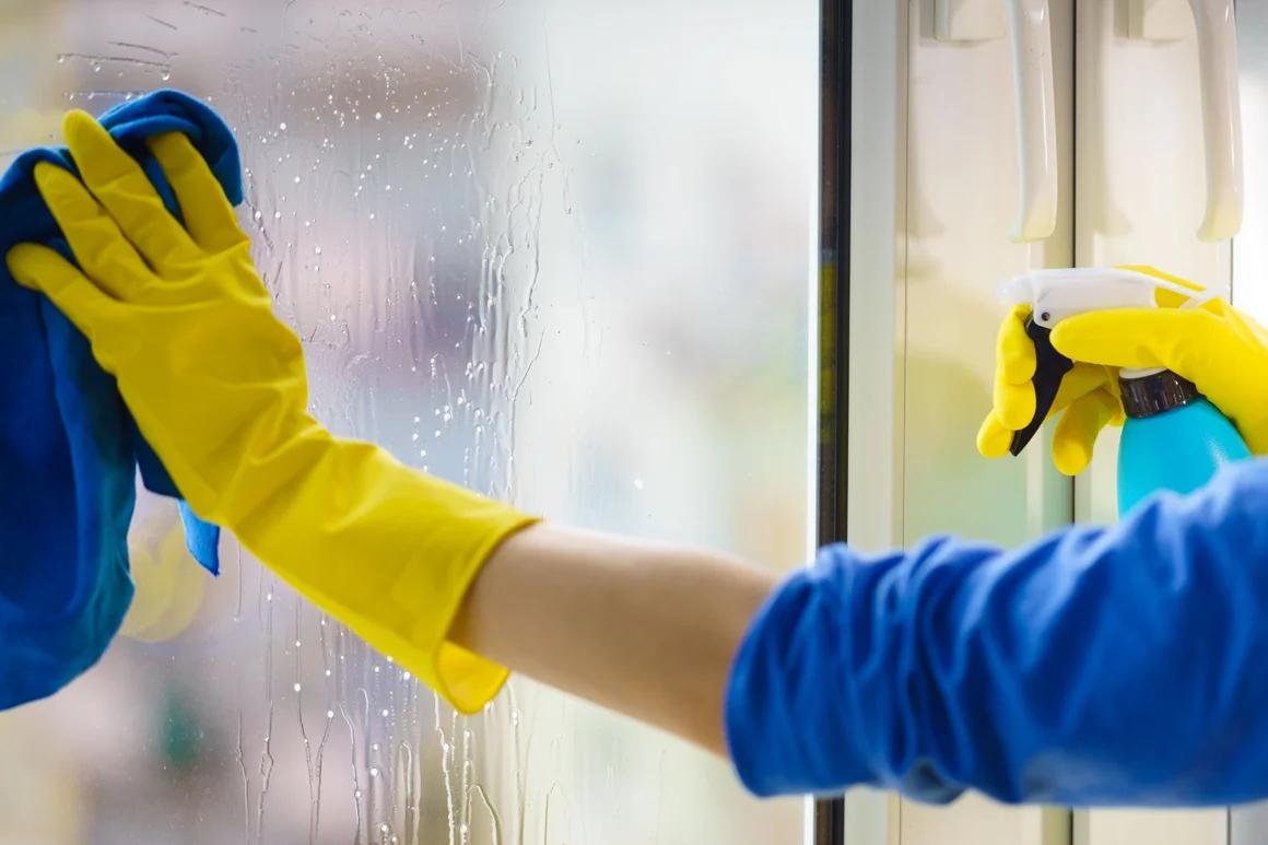 Person reinigt Fenster mit Lappen und Sprühflasche
