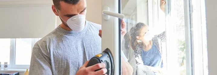Person schleift Fensterrahmen mit Schleifgerät