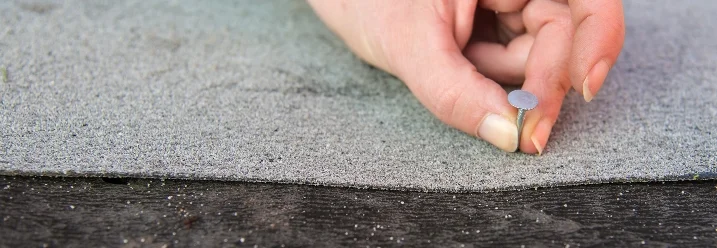 Hand positioniert Nagel auf Dachpappe