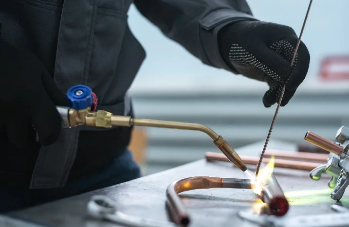 Person lötet Kupferrohre mit Gasbrenner