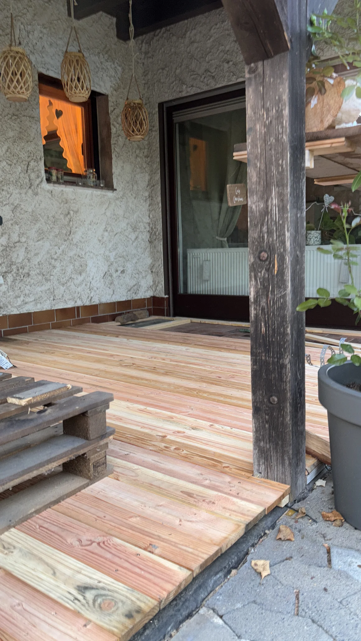 Bau einer neuen Holzterrasse mit hellen Dielen neben einer Hauswand.