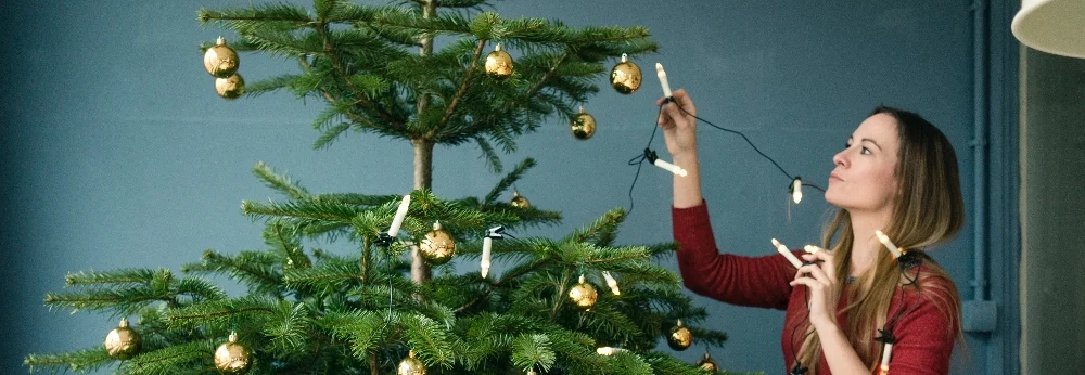 Person schmückt Weihnachtsbaum mit Lichterkette