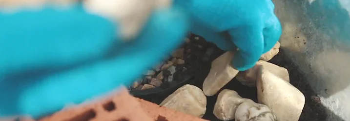 Hand in blauem Handschuh platziert Steine in einem Mini-Teich