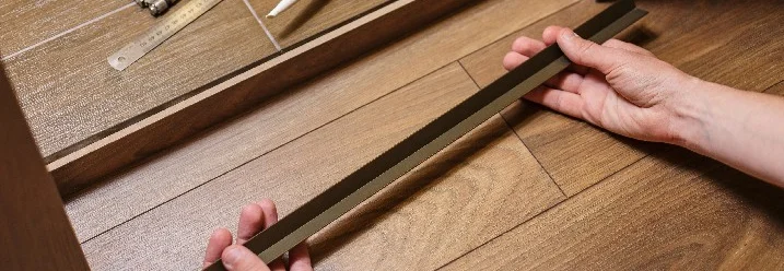 Person hält Metallleiste über Laminatboden