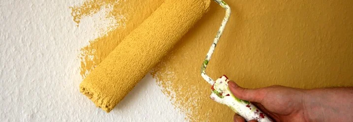 Hand streicht Wand gelb mit Farbrolle
