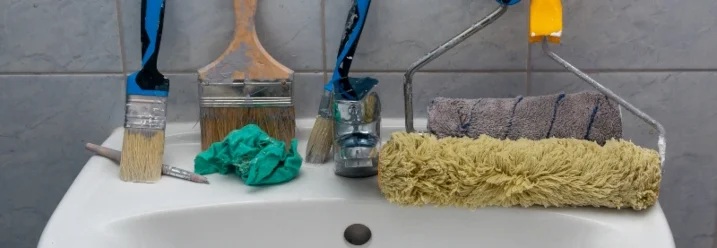 Verschiedene Pinsel und Farbroller in und auf einem Waschbecken.