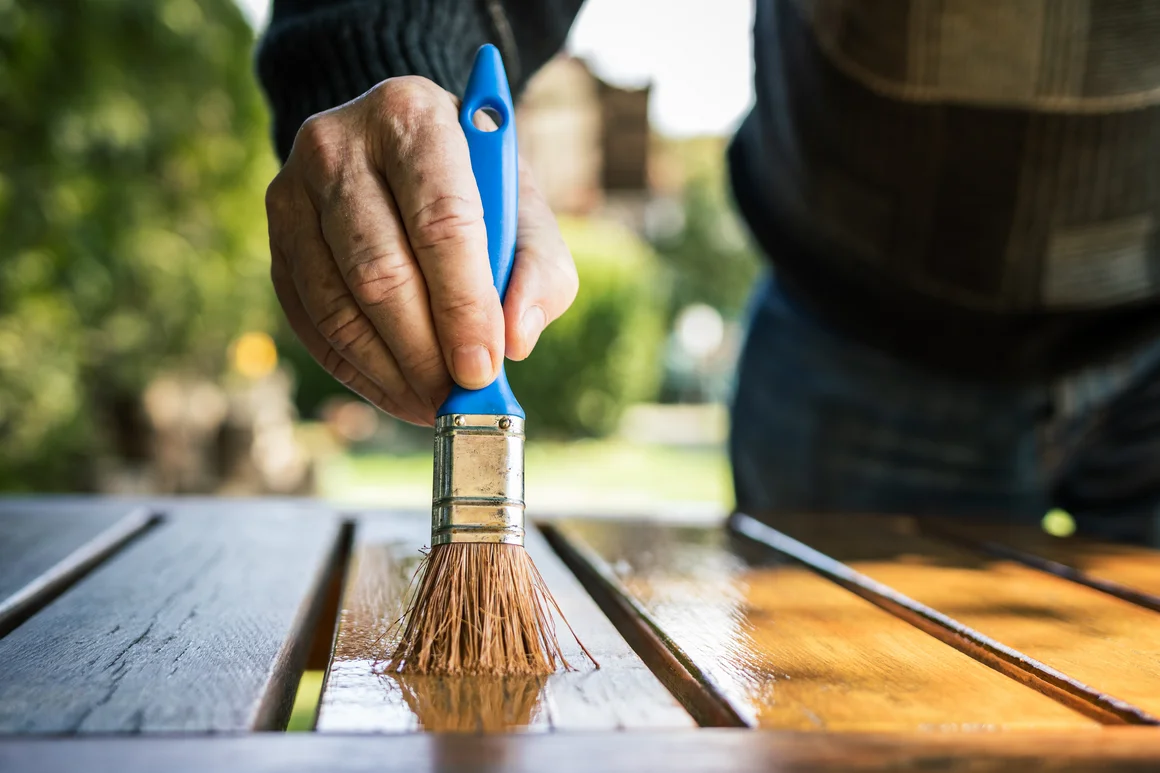 Person streicht Holztisch mit Pinsel