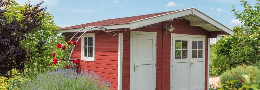 Rotes Gartenhaus mit weißen Türen im blühenden Garten.