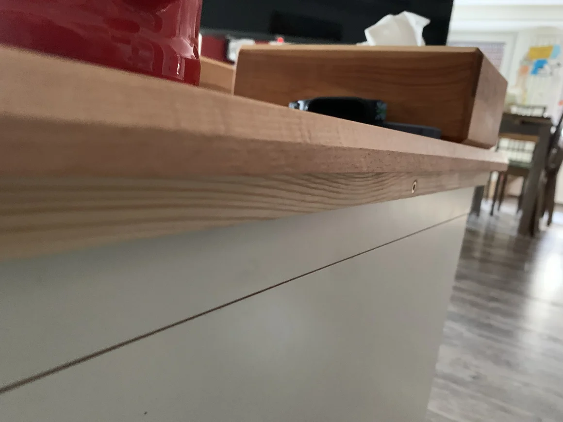 Nahaufnahme der Kante einer Holzplatte auf einem weißen Schrank.