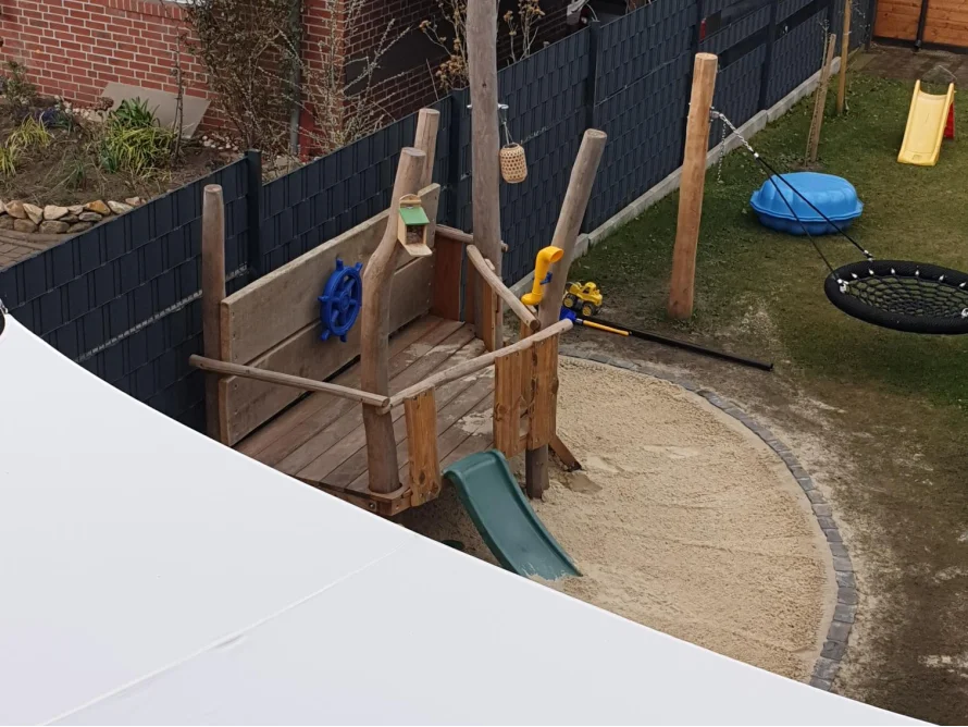 Ein Spielplatz im Garten mit einem Spielturm aus Holz und einer Rutsche. 