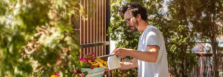 Person gießt Blumen auf einem sonnigen Balkon.