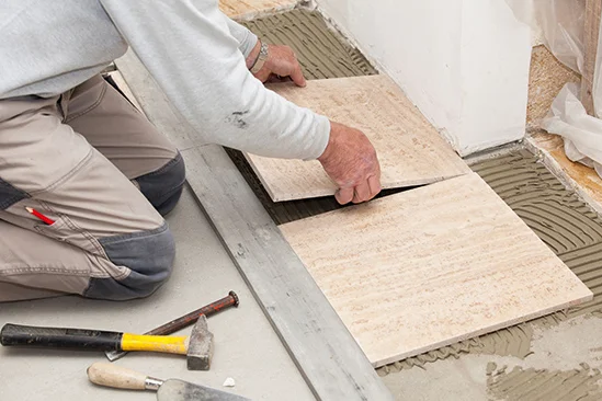 Person verlegt Fliesen mit Fliesenkleber.