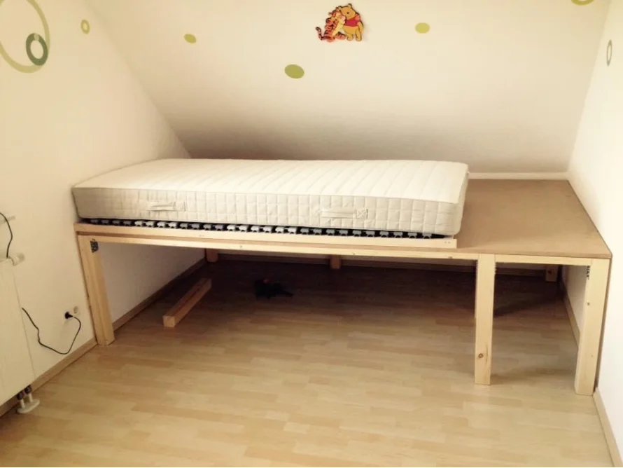 Ein Einzelbett mit Holzrahmen in einem Zimmer mit Dachschräge.