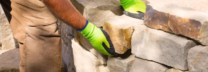 Person baut eine Trockenmauer aus Steinen.