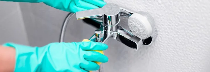 Person reinigt Wasserhahn mit Schwamm