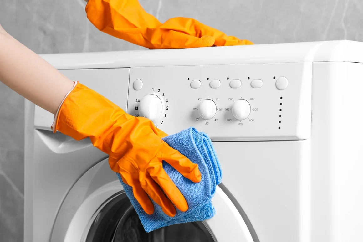 Person reinigt eine Waschmaschine mit einem blauen Lappen.