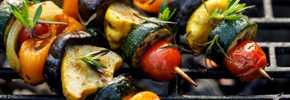 Bunte Gemüsespieße mit Kräutern liegen auf einem Grillrost.
