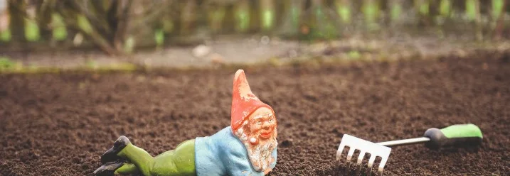 Ein Gartenzwerg und eine Harke liegen auf der Erde