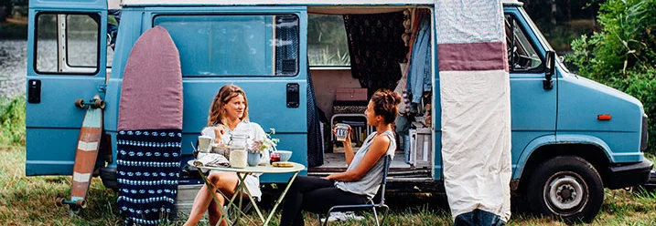 Zwei Personen sitzen vor einem Campingbus.