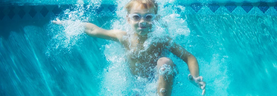 Kind mit Schwimmbrille taucht im Pool