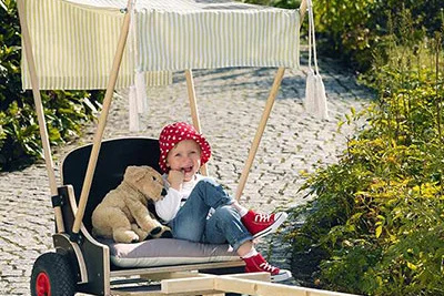 Kind sitzt in einem Holzbollerwagen mit Sonnensegel