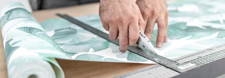 Person schneidet Tapete mit Cuttermesser