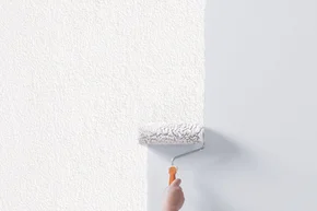 Hand trägt weiße Farbe mit Rolle auf