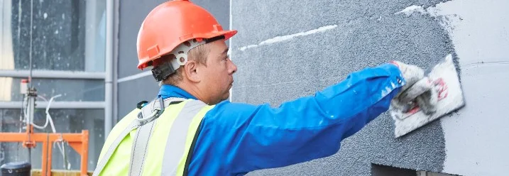Person verputzt Hauswand mit Kelle.