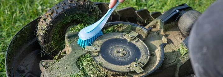 Person reinigt Rasenmäher mit Bürste