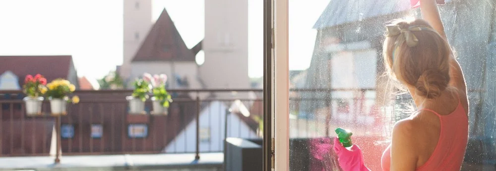 Person reinigt Fenster mit Sprühflasche