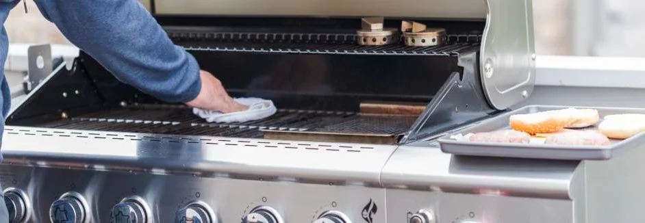 Person reinigt Gasgrill mit Tuch.