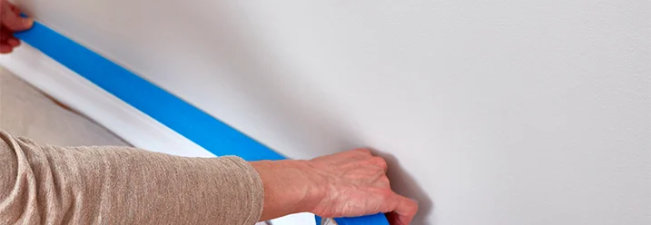 Person klebt Malerband an eine Wand