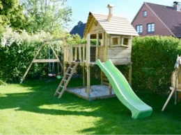 Ein Holzhäuschen mit Rutsche und Schaukel auf einem Rasen.