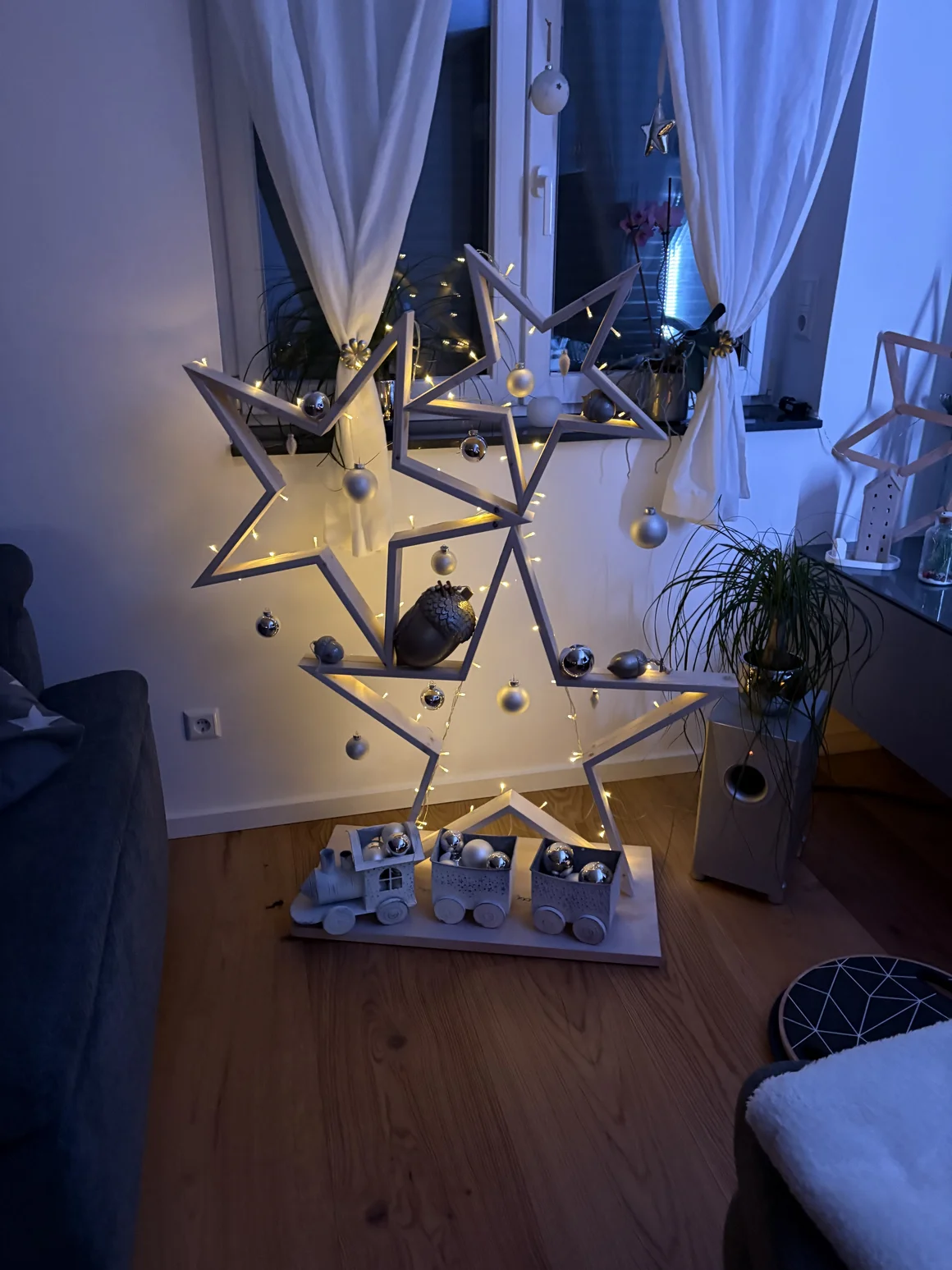 Ein beleuchteter, hölzerner Stern ist weihnachtlich mit Kugeln dekoriert.