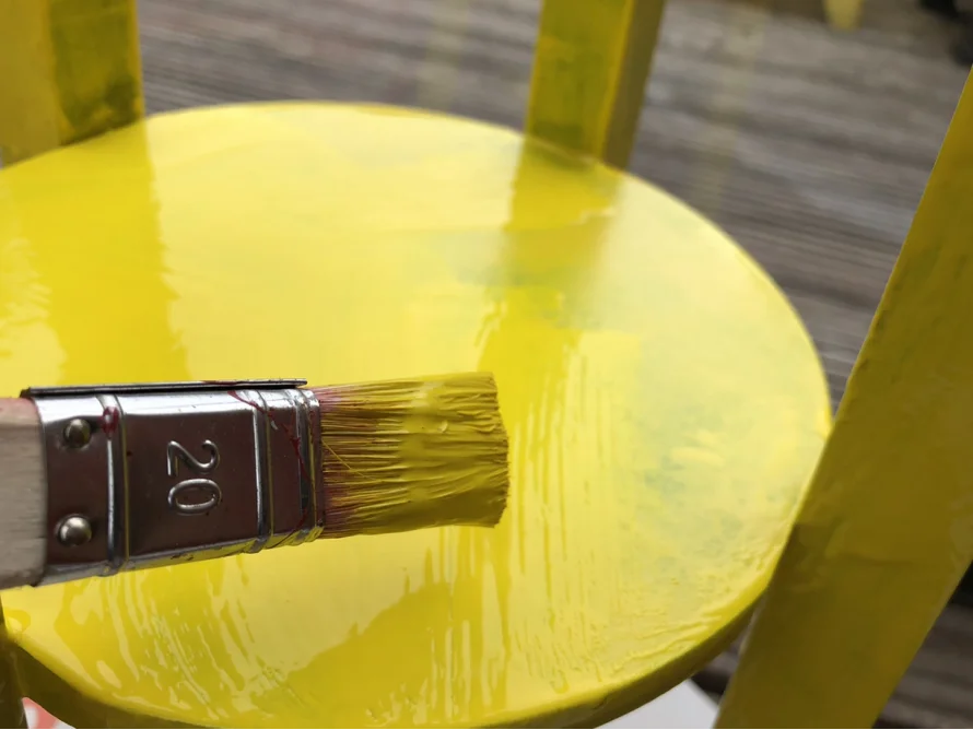 Pinsel trägt gelbe Farbe auf Holz auf