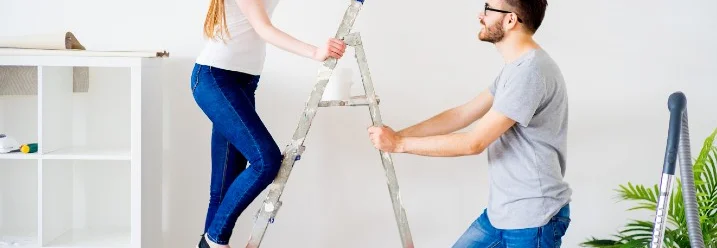 Eine Person steht auf einer Leiter, die von einer anderen Person festgehalten wird.