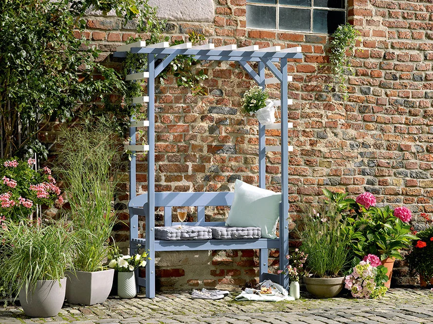 Blaue Holzbank mit Pergola an einer Backsteinmauer