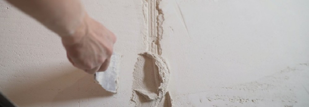 Hand trägt Spachtelmasse an Wand auf