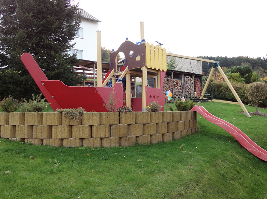 Ein Spielplatz im Garten mit einem Spielgerüst in Form eines Schiffes und einer Rutsche